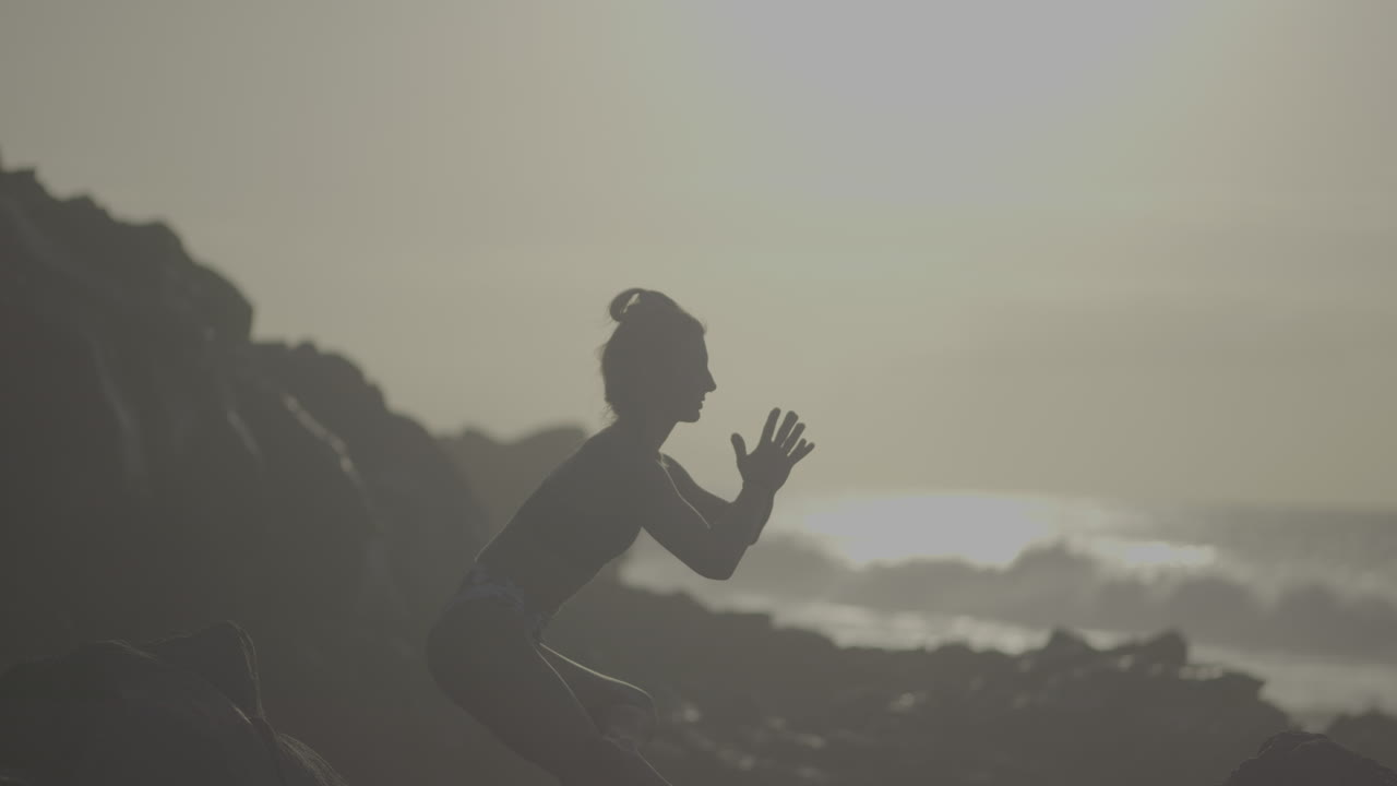 Woman practicing yoga on a rocky beach at sunrise