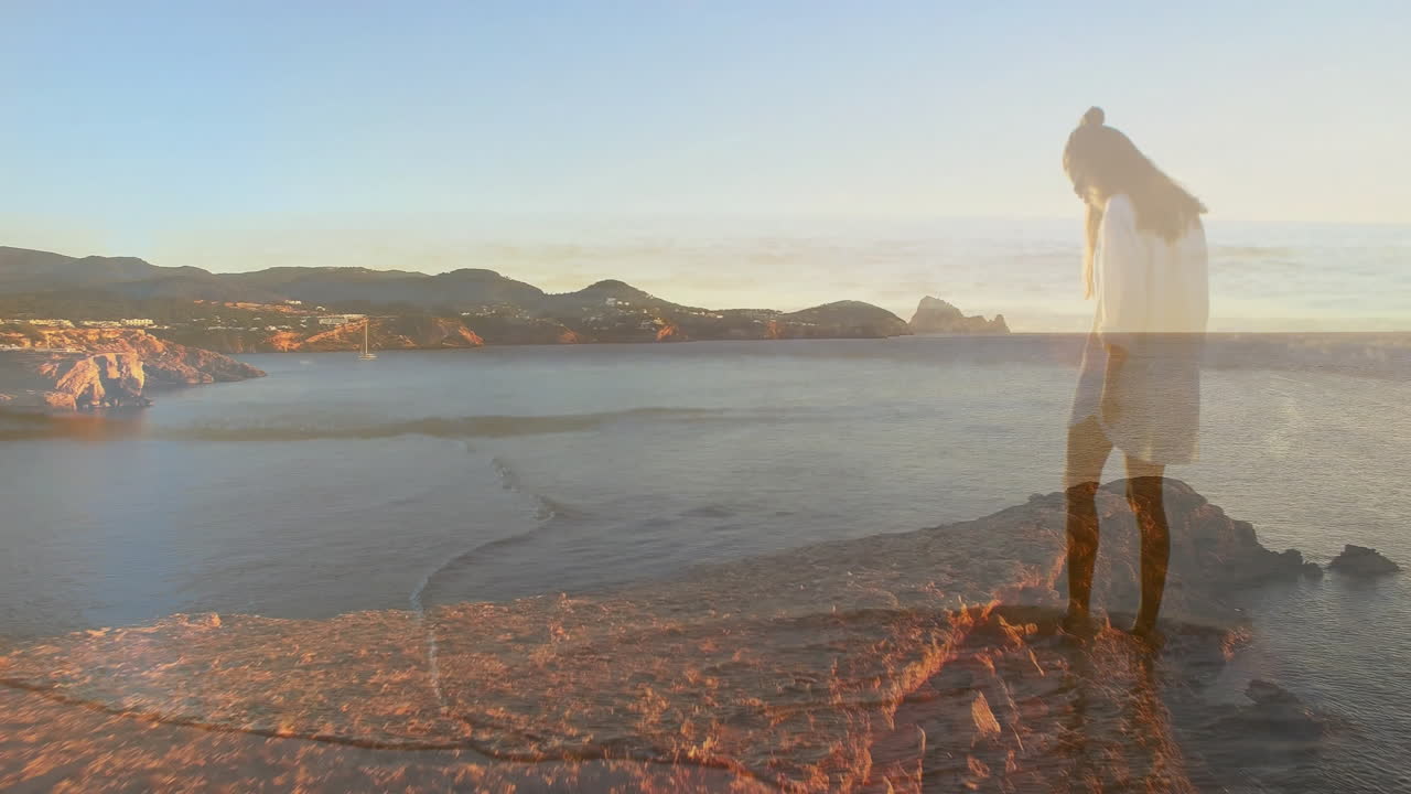 Standing on rocky cliff, woman overlooking calm ocean and distant hills animation
