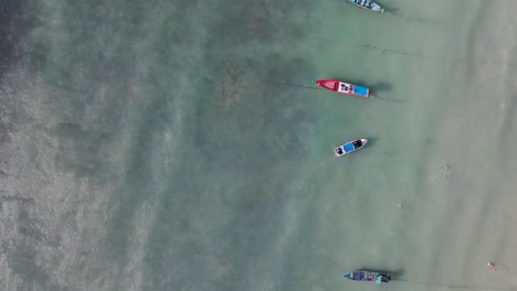 Luftaufnahme-Aus-Der-Vogelperspektive-Entlang-Einer-Reihe-Festgemachter-Leerer-Boote-Vor-Dem-Strand-Von-Sairee-In-Seichten-Gewässern