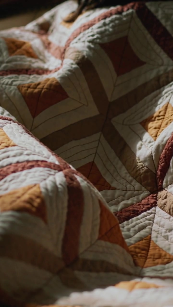 Video verticale: Persona che respira e si muove sotto una trapunta patchwork in una piccola camera da letto, rivelando i capelli