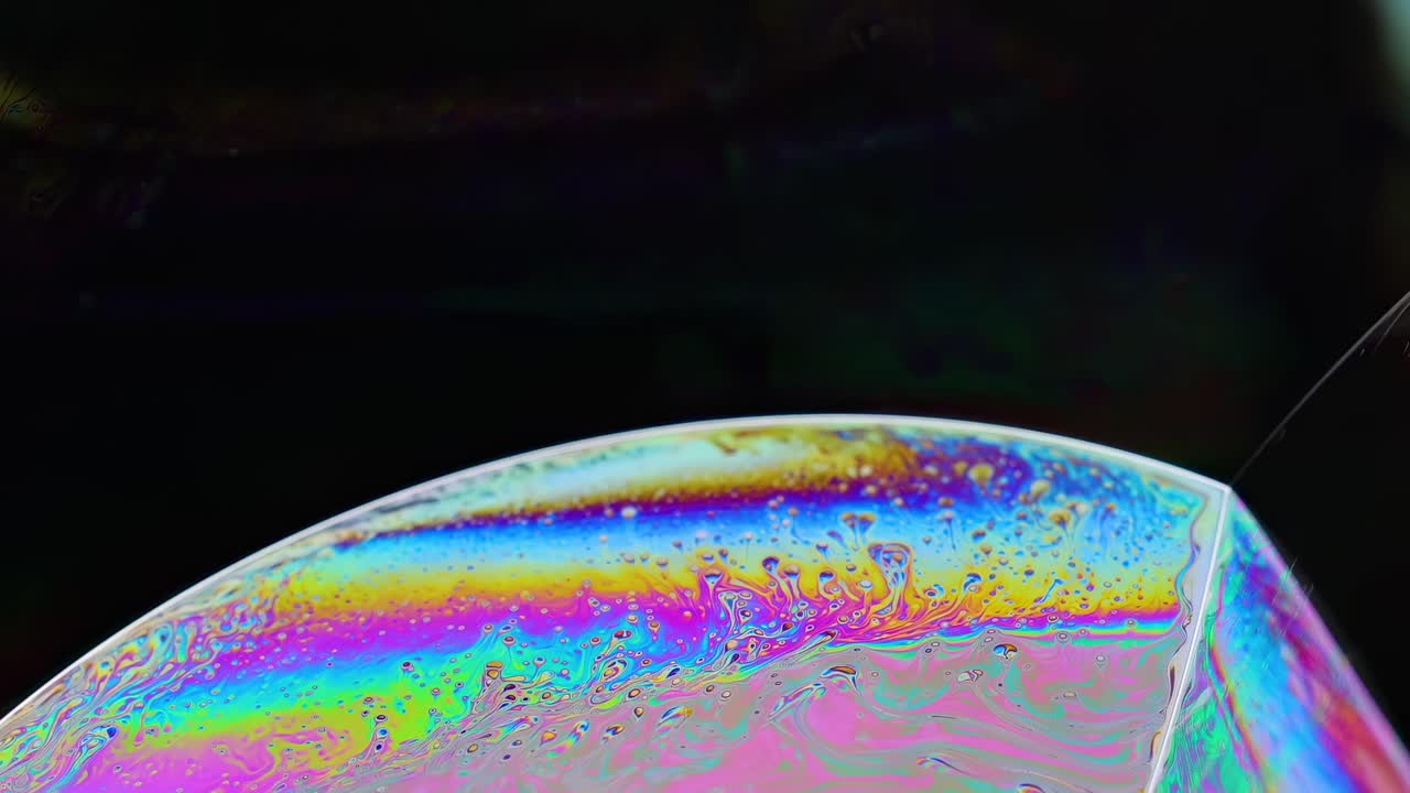 Detailed view of a soap bubble's colorful surface patterns against a dark backdrop, showcasing vibrant iridescence.
