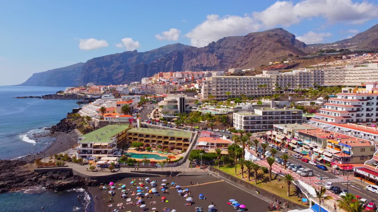 una lenta toma cinematográfica que se inclina hacia abajo para ver la playa de la arena con la ciudad de santiago del teide en el fondo