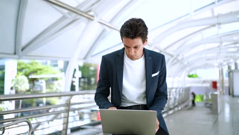 confident businessman using laptop working outdoors in the financial district in the city. using phone talking to client solving problems