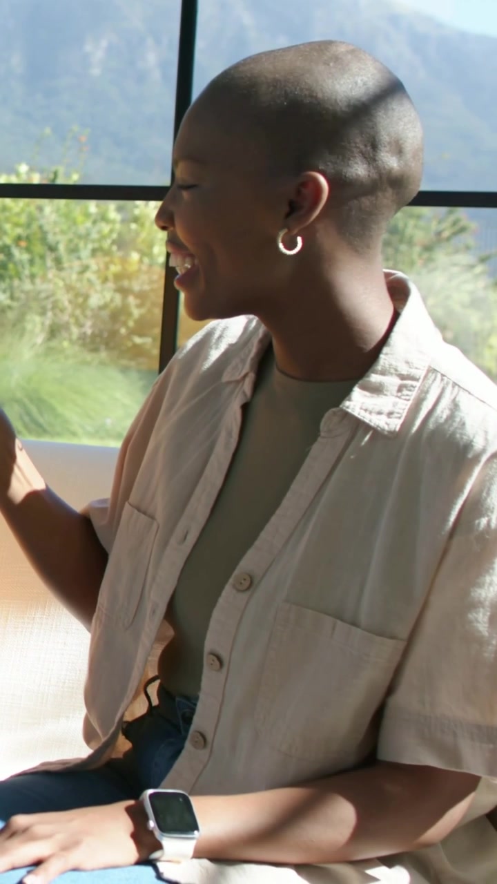 Vertical video: Reacting to remark, woman raising pink mug laughing by grid window in beige shirt