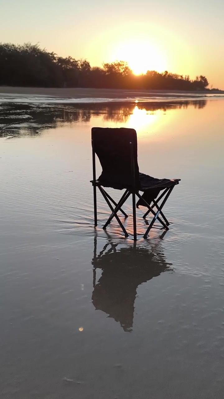 Sedia pieghevole vuota in piedi nell'acqua bassa della spiaggia al tramonto.