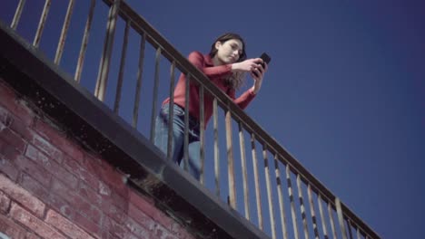 Girl-leaning-on-a-railing-using-the-smartphone-in-slow-motion-with-blue-sky-in-the-background