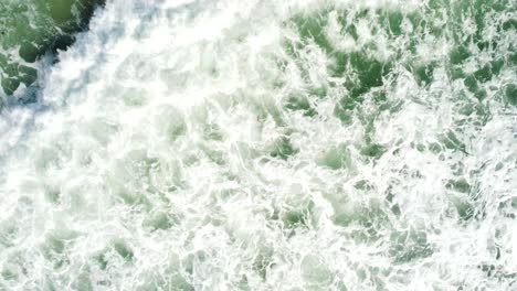Crashing-tropical-wave-leaving-white-foam,-aerial-top-down-descend-view
