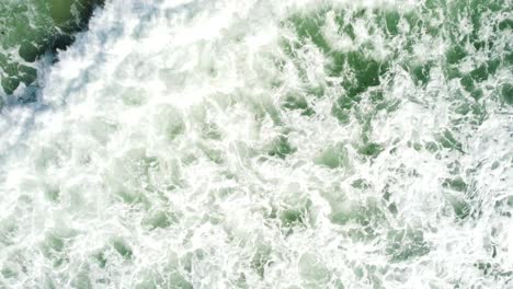 crashing tropical wave leaving white foam, aerial top down descend view