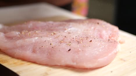 pecho de pollo crudo sazonado con sal y pimienta en una tabla de cortar