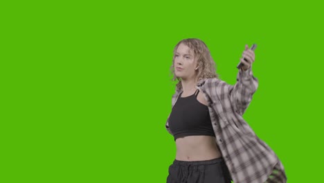 studio shot of young woman listening to music on mobile phone and dancing against green screen 2