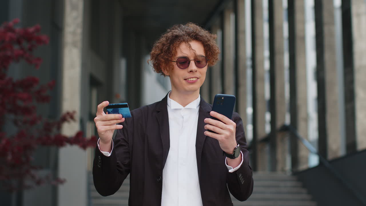 Un uomo d'affari felice che usa uno smartphone e una carta di credito per fare acquisti online in piedi in una strada della città