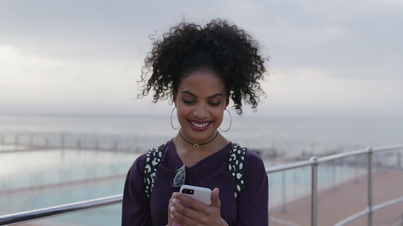 ritratto di una giovane donna attraente che usa i messaggi telefonici sorridendo felice sulla spiaggia
