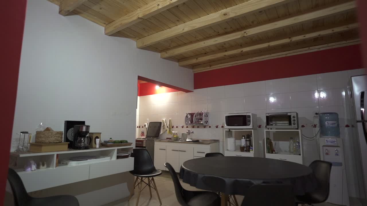 Left opening general pan view of rustic house kitchen, with white and read walls, wooden ceiling and round black table. Broad spaces. Shot on 4K.