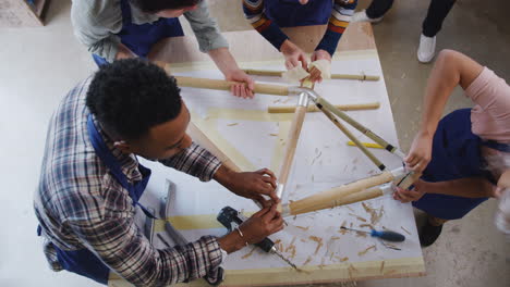 Overhead-Shot-Of-Multi-Cultural-Team-In-Workshop-Assembling-Sustainable-Bamboo-Bicycle-Frame