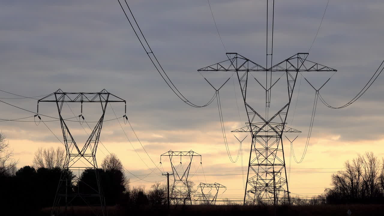 Electrical transmission towers stretch into distance against somber cloudy sky at sunset