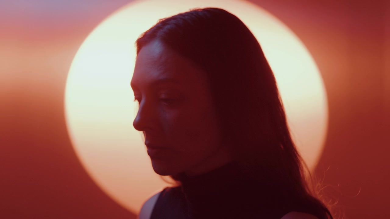 Donna contemplativa di profilo davanti a una luce circolare luminosa.