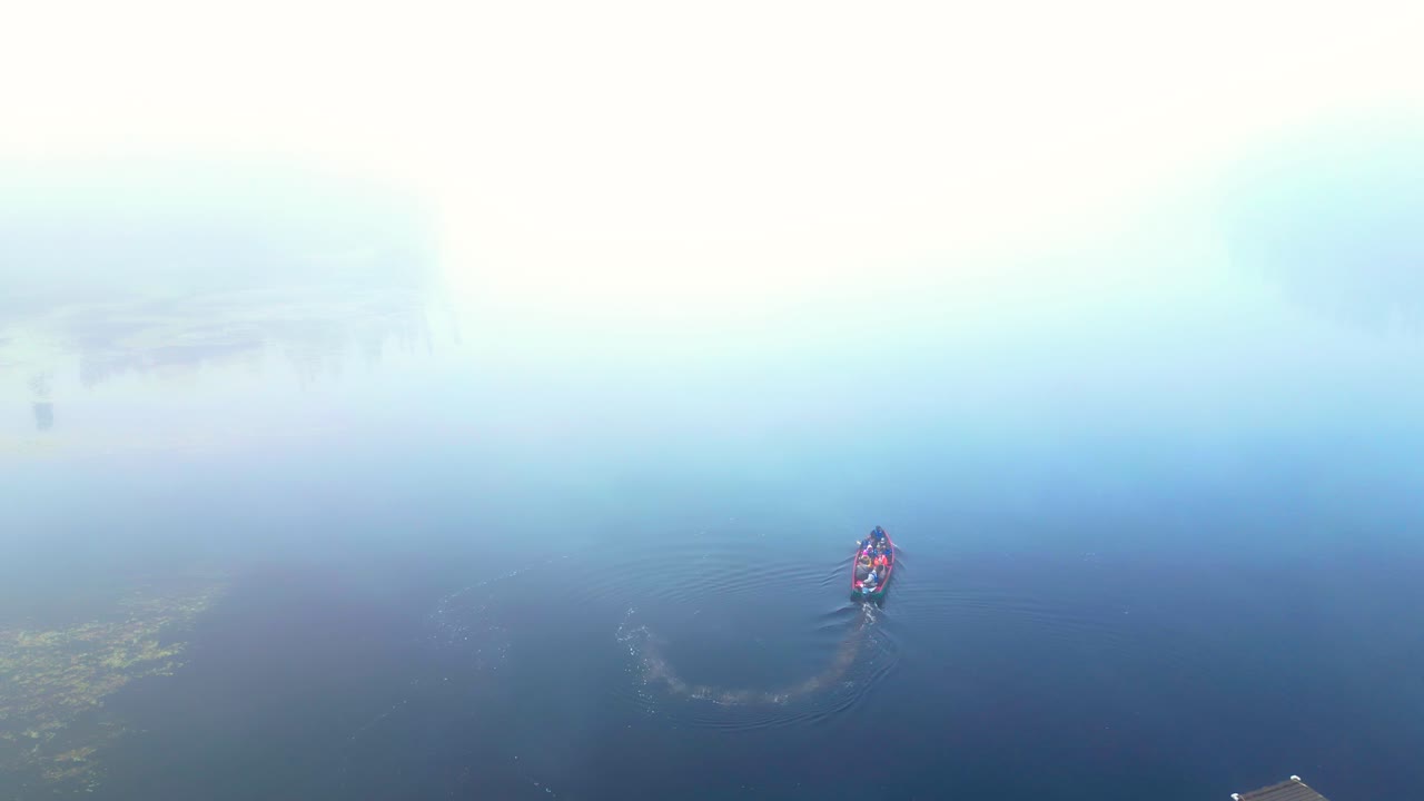 Vista aerea di una piccola barca che si muove nella fitta nebbia su un fiume tranquillo, circondato da una foresta selvaggia, la nebbia svanisce all'orizzonte