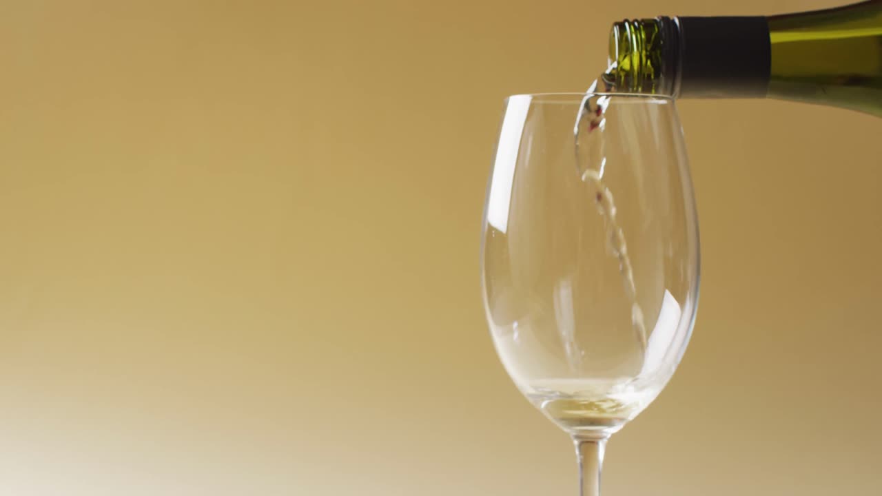 Vino bianco versato in un bicchiere su sfondo giallo con spazio di copia.