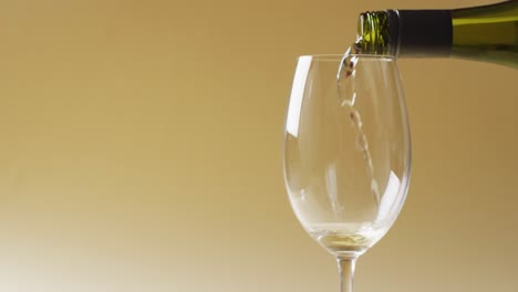 white wine pouring into glass over yellow background with copy space