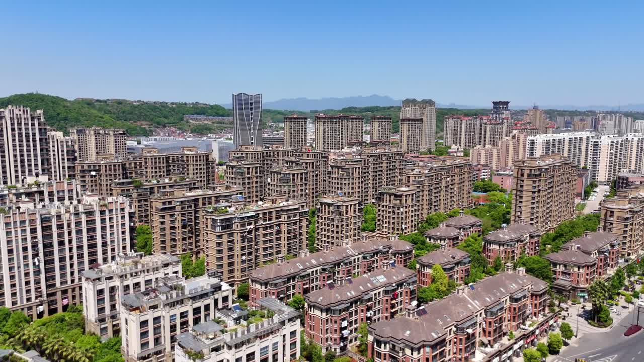 Aerial view of a dense residential complex in Shaoxing, Zhejiang Province, showcasing modern mid-rise apartment buildings surrounded by greenery and distant hills under a clear blue sky. China. UHD.