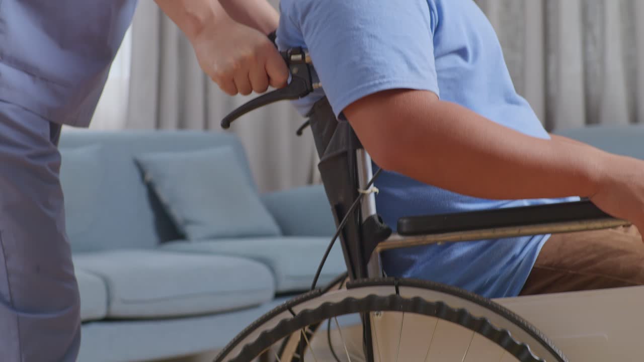 남자 간호사가 체어에 앉은 환자를 집에서 물리 치료를 받은 후 다른 방으로 밀어넣는 장면