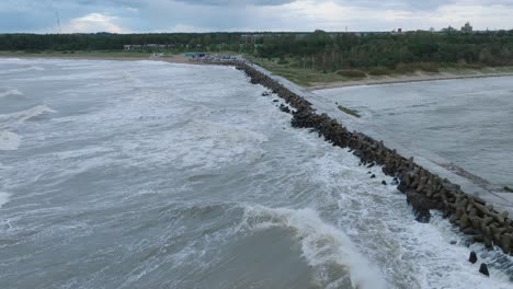 aerial establishing view of port of liepaja concrete pier , autumn storm, big waves splashing, overcast day, wide drone shot, pano right