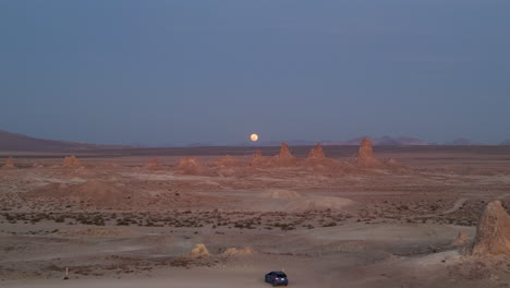 an aerial view of a full moon rising over a desert landscape revealing a parked blue car