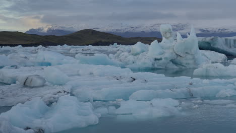 Glacier-Lagoon,-Jökulsárlón,-Iceland,-showcasing-icebergs-in-icy-blue-water-with-snowy-mountains-in-the-background