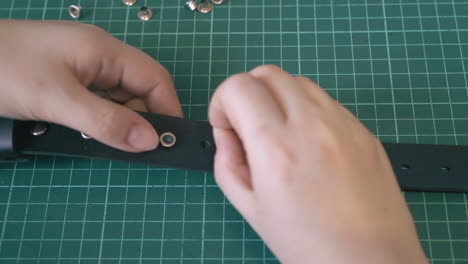 skilled tailor puts silver eyelets into leather belt holes