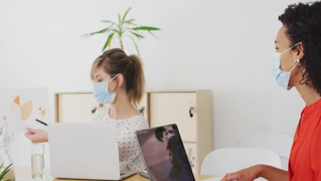 mujer con máscara facial mostrando un documento a su colega en la oficina