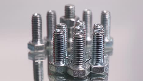 rotating group of galvanized metallic screws close-up. stainless steel bolts isolated on mirror reflective background.