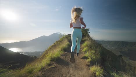 Fit-sportive-woman-running-on-ridge-of-mount-Batur-towards-edge,-raising-arms-into-air,-high-on-life,-freedom