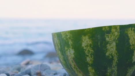 half of ripe watermelon on the pebbles in the beach with splashing waves on the background in greece