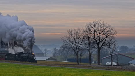 a view of an antique restored steam passenger train approaching in the early morning blowing steam on a winter day