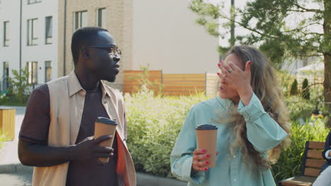 multiethnic man and woman walking with coffee in park and talking