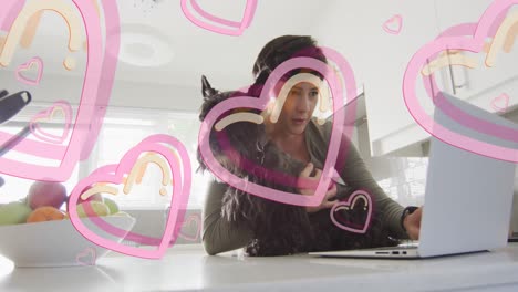 Animation-of-hearts-over-caucasian-woman-using-laptop-with-her-pet-dog