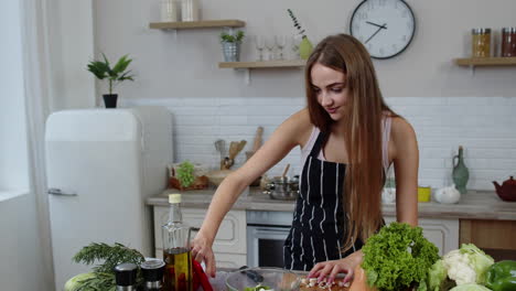 Vegan-girl-cooking-salad-with-raw-vegetables-while-looking-on-mobile-phone-for-online-recipe