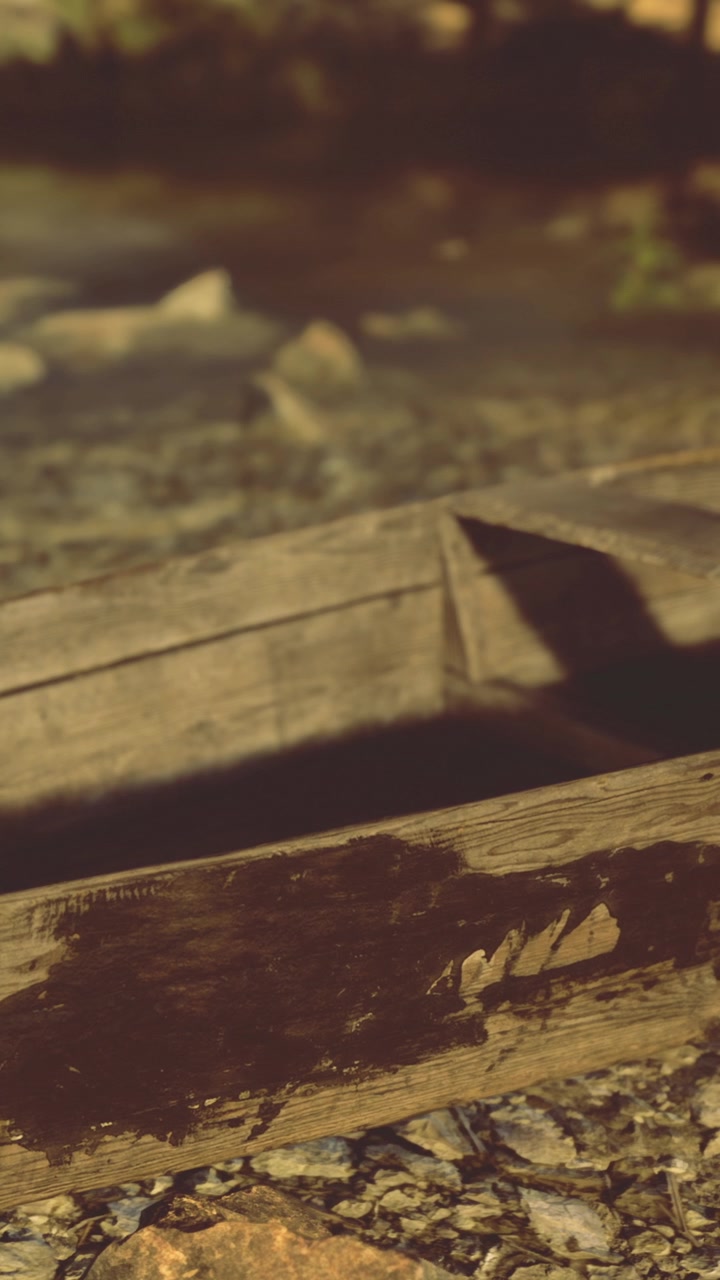 Gammel træbåd hviler ved flodbredden under den gyldne time nær roligt vand.