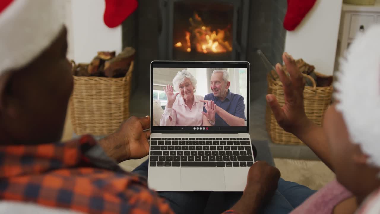 pareja afroamericana con sombreros de santa usando una computadora portátil para una videollamada de navidad con la pareja en la pantalla