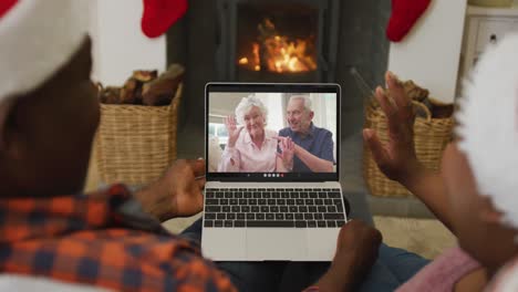 African-american-couple-with-santa-hats-using-laptop-for-christmas-video-call-with-couple-on-screen