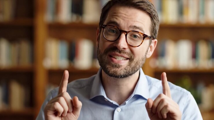 Un oratore amichevole che interagisce con un pubblico in un'accogliente ambientazione da biblioteca, mostrando entusiasmo e calore attraverso un sorriso genuino e un gesto accogliente.