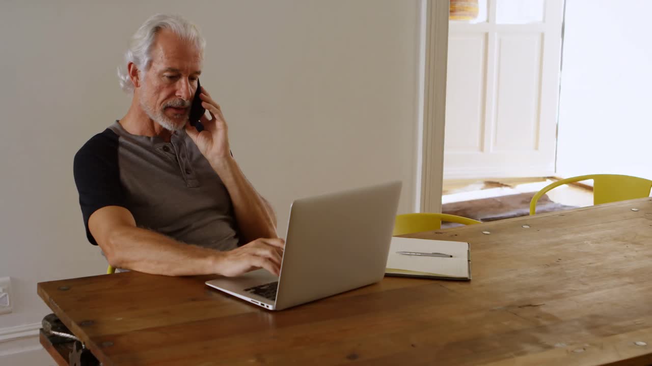 Ældre mand, der taler i mobiltelefon, mens han bruger bærbar computer 4k