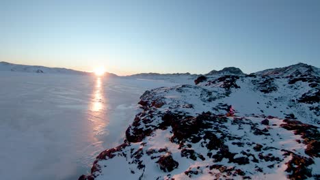 drone fpv volando sobre el terreno congelado hacia la puesta de sol junto a los acantilados