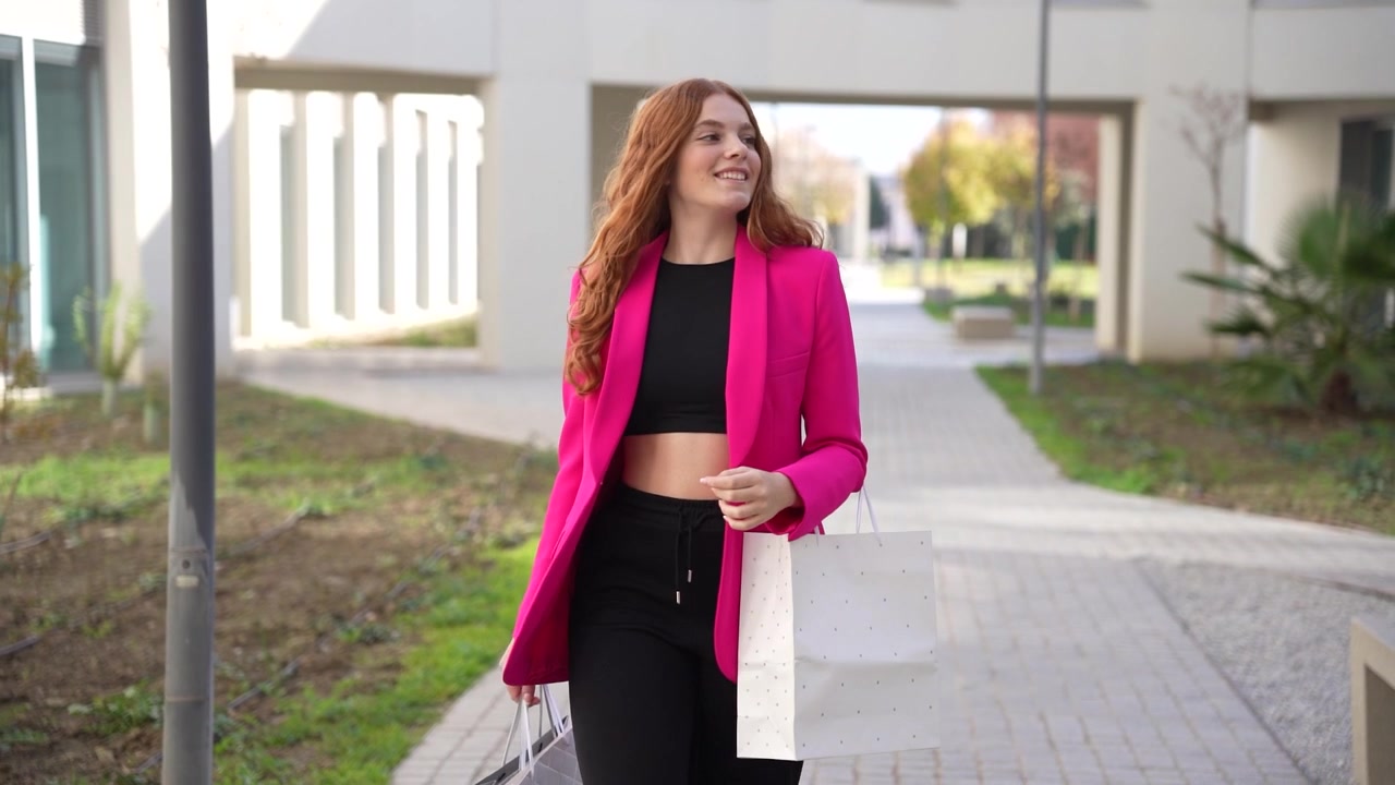 En selvsikker forretningskvinde klædt i en stilfuld pink blazer går yndefuldt udendørs.