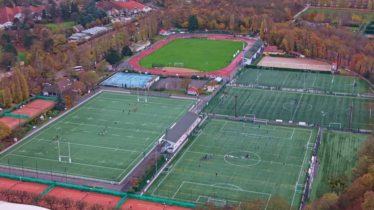 Aerial view of a large, comprehensive sports complex featuring natural and artificial turf pitches, a running track, rugby and football fields