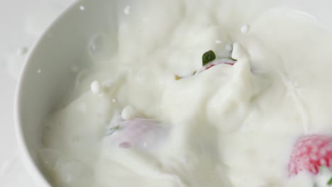 two strawberries falling into bowl of milk in slow motion