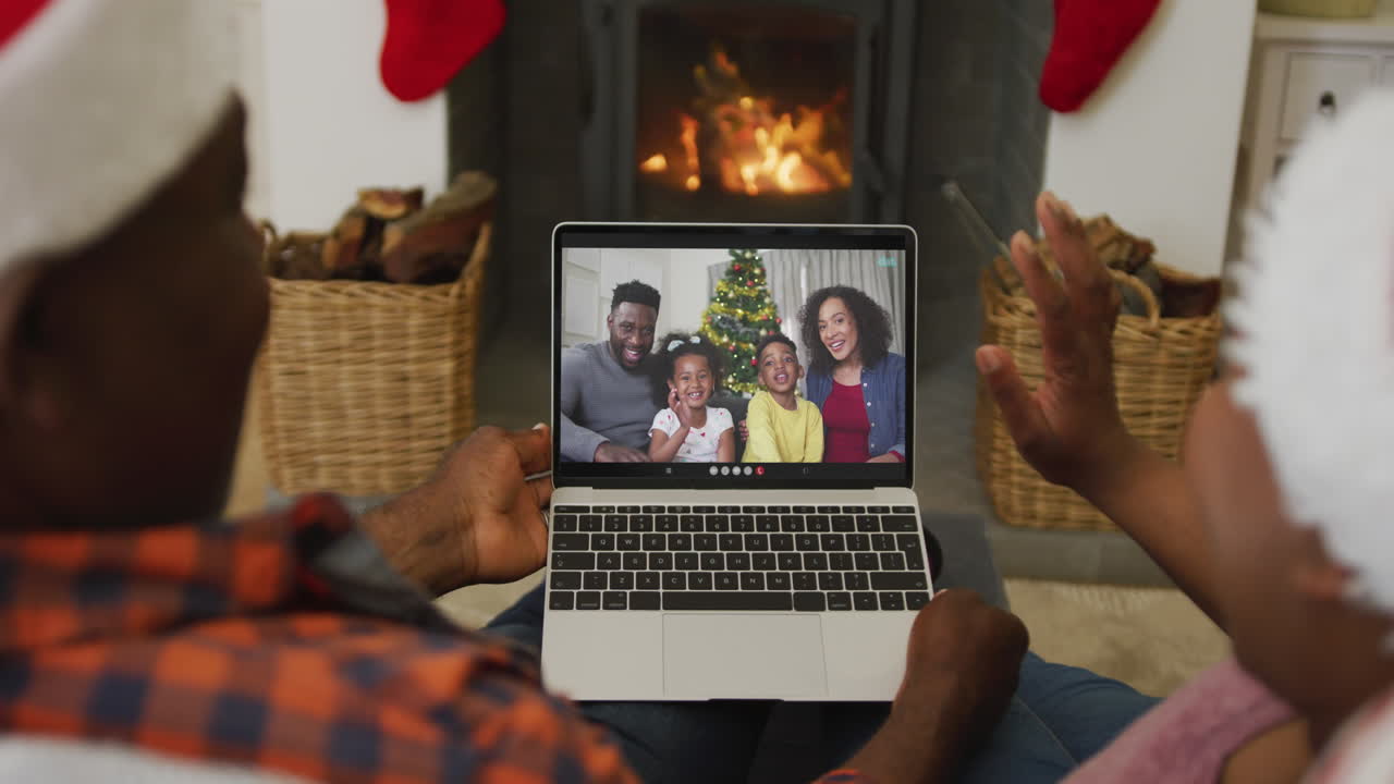 una pareja afroamericana con sombreros de santa usando una computadora portátil para una videollamada de navidad con la familia en la pantalla
