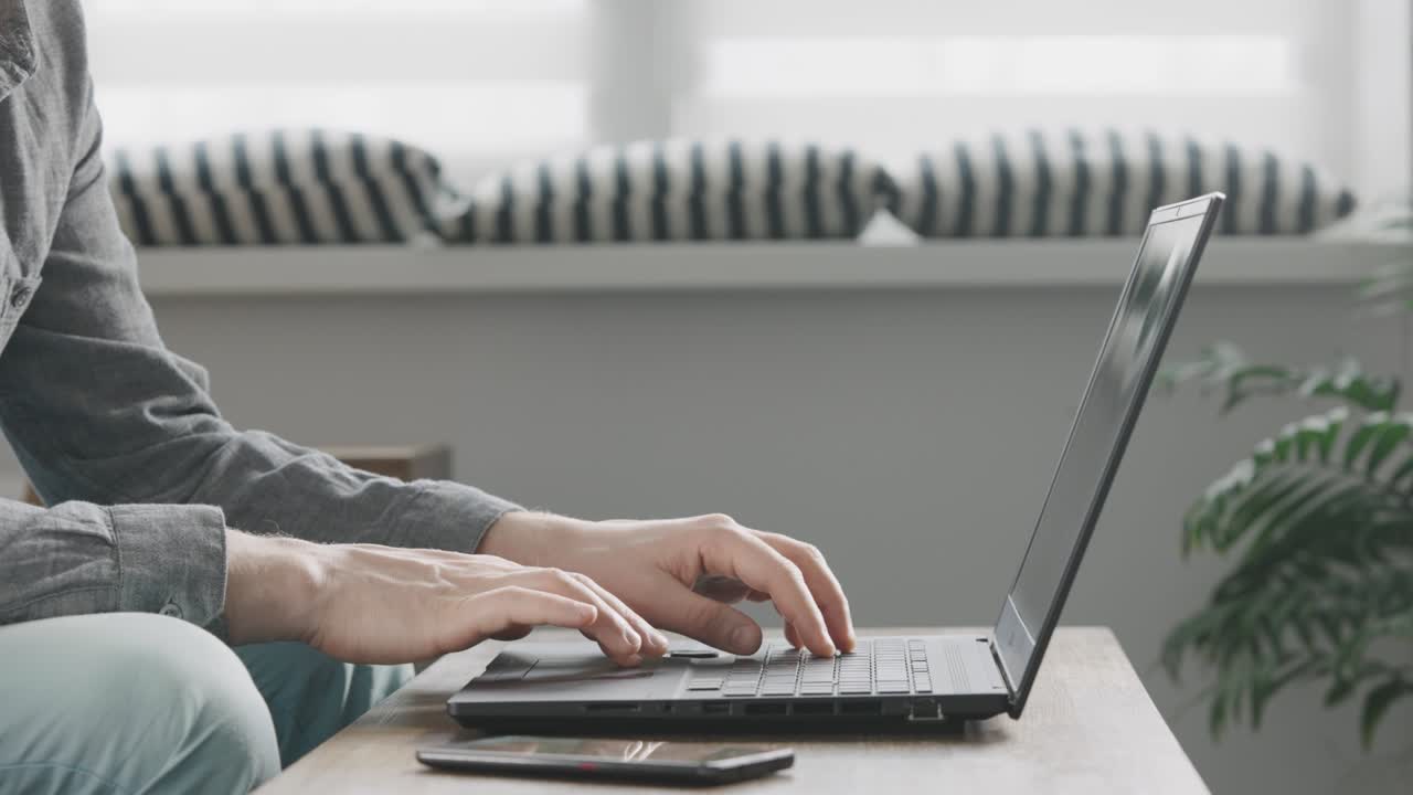 인식할 수 없는 남자가 집에서 일하기 위해 노트북을 사용합니다.