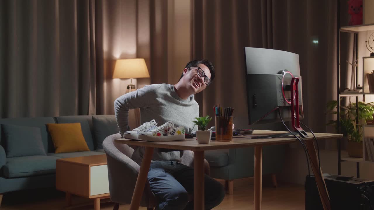 아시아 남성 신발 디자이너가 집에서 데스크 컴퓨터에서 일하면서 허리 통증에 시달리고 있습니다.