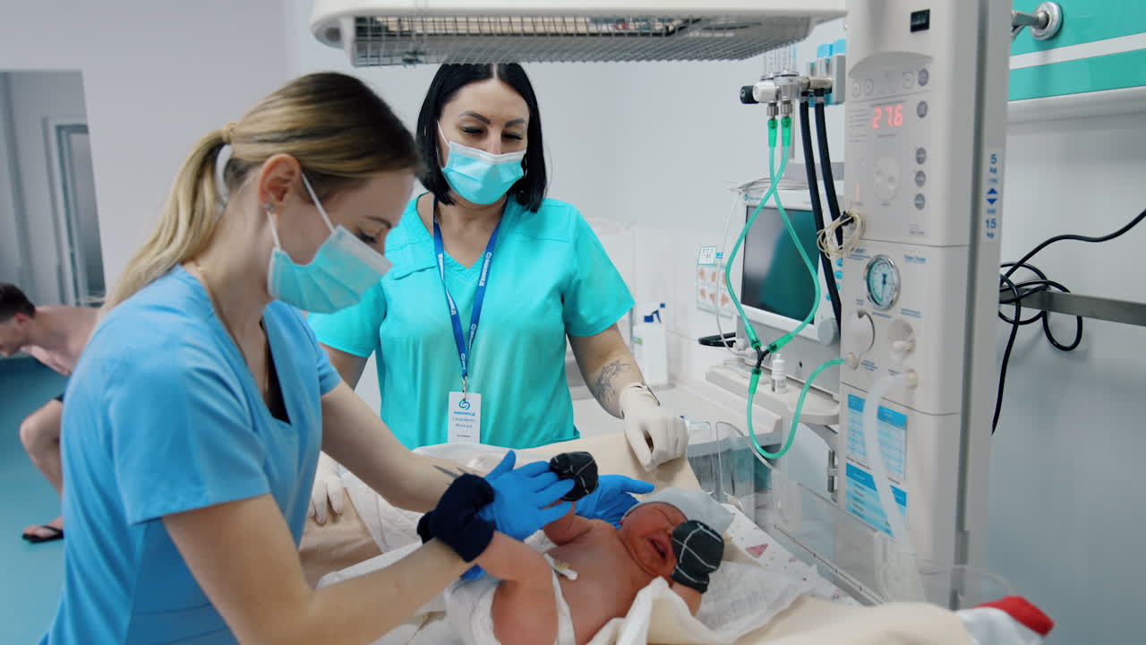 Medics take care of a newborn baby. Nurse takes off little mittens and cap from a child. Check up after birth.